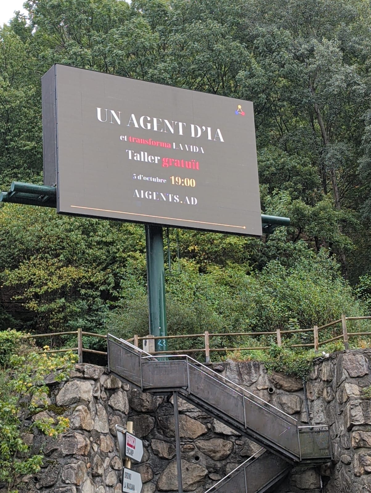 A billboard in Andorra. The board reads UN AGENT D'IA, Taller gratuït, 5 d'octubre 19:00, AIGENTS.AD.